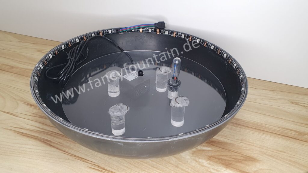 Abbildung 4 zeigt die Brunnenschale mit eingesetzter Brunnenplattform, dem eingebauten Wasserstandsanzeiger, der Brunnenpumpe und dem LED-Streifen.