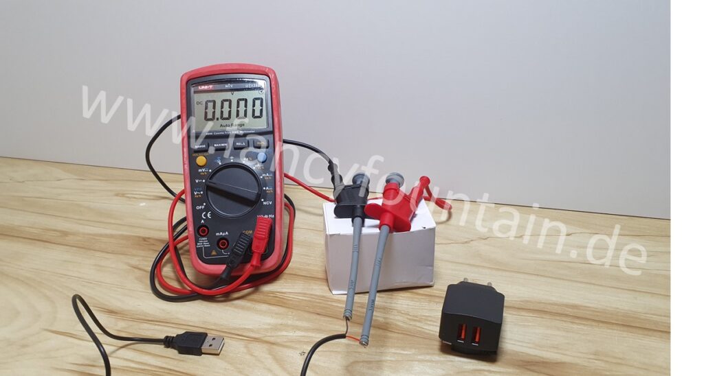 Zum Versuchsaufbau zur Spannungsmessung gehören ein Miltimeter, Messspitzen, das USB Steckernetzteil und das USB-Kabel was auf diesem Bild dargestellt ist.